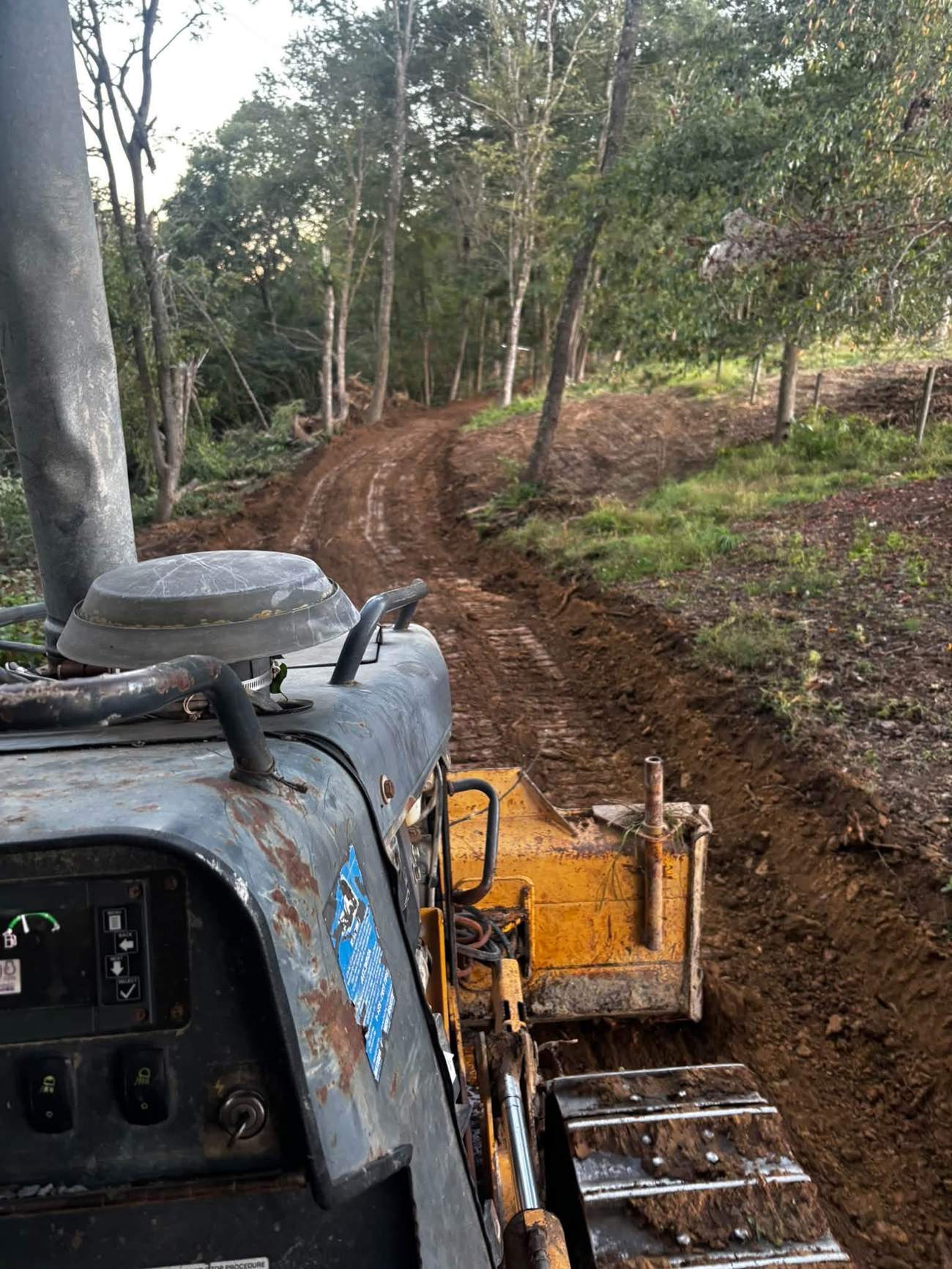 Excavator grading a dirt access path through wooded property